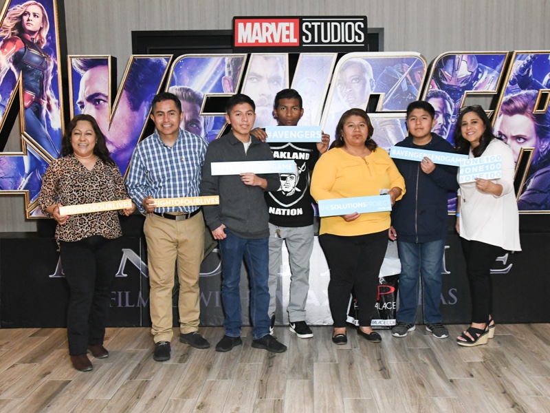 Seven people posing on front of a Marvel Studios sign